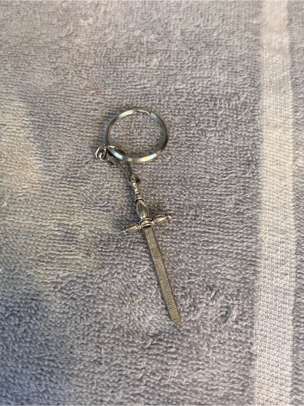 Medieval sword keychain features an intricate hilt and a textured blade pendant.